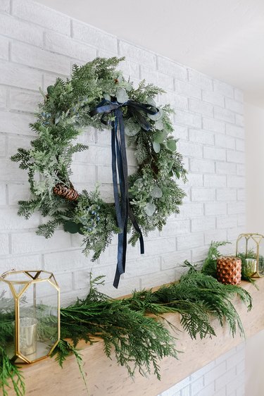 Winter wreath with navy blue bow above Christmas mantel