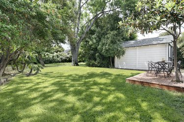 a green lawn with a deck platform; green trees surround a two-car garage