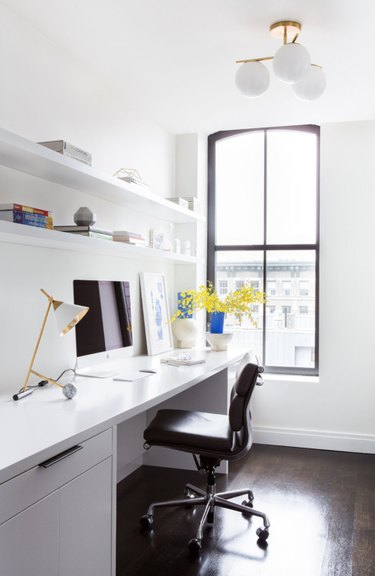 Home Office Organization Ideas with White desk, black desk chair, brass desk lamp, white shelves, white globe light.