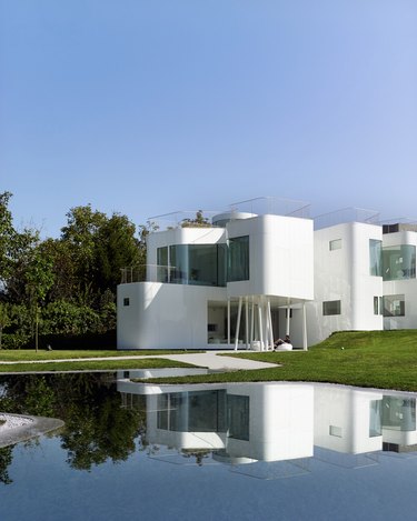 Bauhaus style residence with white exterior and large windows next to pond