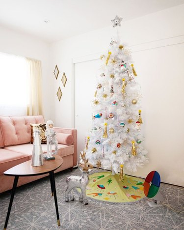 White Christmas Tree Ideas with White artificial Christmas tree with mod ornaments and skirt, pink couch, mod coffee table, mod floor tiles, white walls.