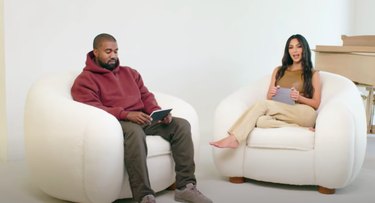 Kanye West and Kim Kardashian-West sitting in white chairs with piano in the background