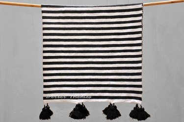 Black-and-white-striped throw blanket with black pom-poms on two sides
