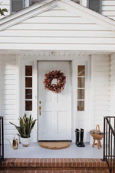 Freshly painted concrete porch with gray paint, wreath on door, entry rug, planter, boots and watering can