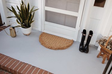 Rug, plant, boots and watering can on concrete porch painted gray