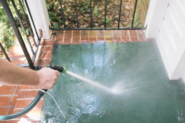 Rinsing concrete porch clean with water hose