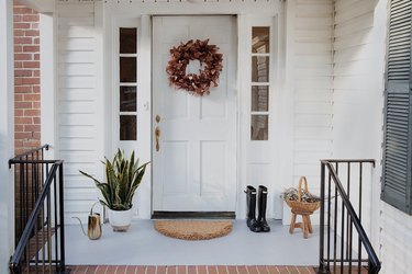 Freshly painted concrete porch with gray paint, wreath on door, entry rug, planter, boots and watering can