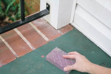 Sanding chipped paint spot on concrete porch