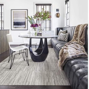 dining room rug idea with carpet tile beneath sculptural table and channel-tufted bench