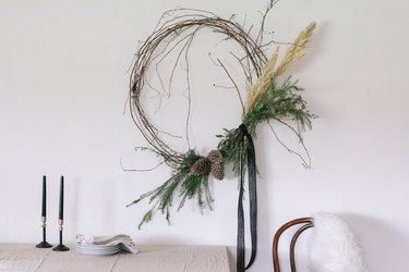 Rustic winter wreath with pampas grass and greens hanging on wall over table.