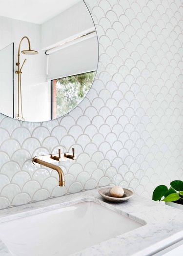 white bathroom countertop idea with marble and fishscale wall tile with wall-mounted faucet