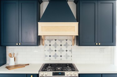 Kitchen with blue cabinets, white tile backsplash, and patterned tile behind stove