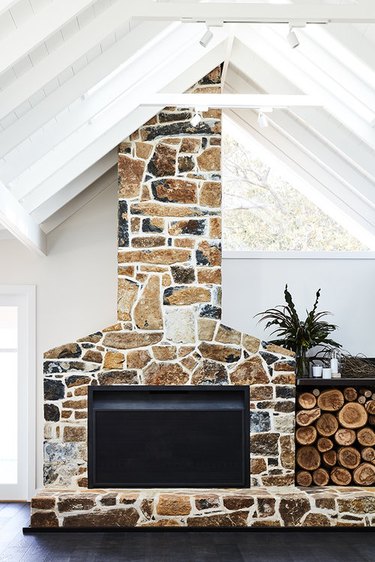 stone fireplace with stacked wood and A-frame ceiling