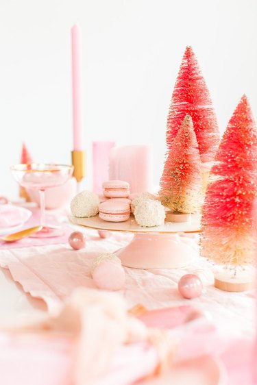 Modern Christmas decor with pink bottle brush Christmas trees, pink cake stand, pink candles, and macaroons