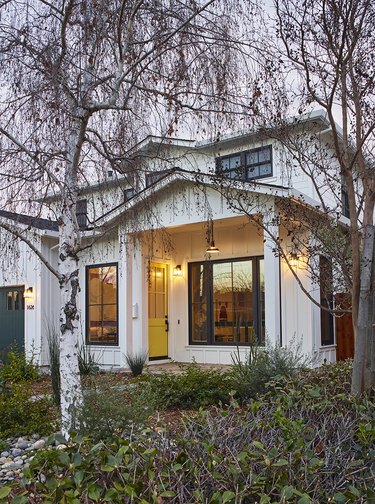 Farmhouse exterior with green trim, white house, trees.