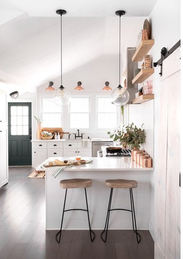 Small kitchen with island, bar stools, white cabinets, pendant lights.