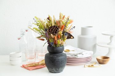 Dried floral arrangement with black clay vase on table with dishes.