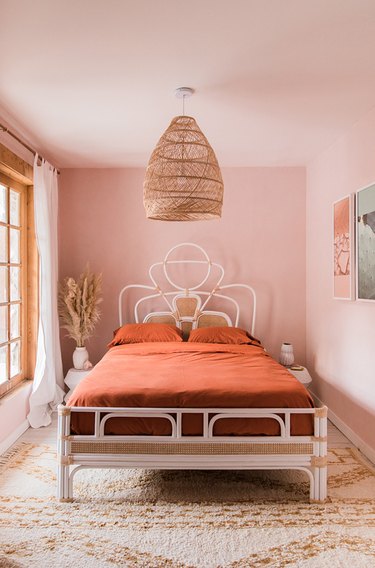 Sunset-hued pink bedroom with woven bohemian pendant and rattan bed frame