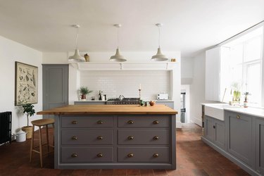 gray cabinets with farmhouse sink and terra cotta kitchen flooring