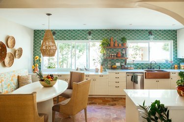 green tile backsplash with white cabinets and terra cotta kitchen flooring