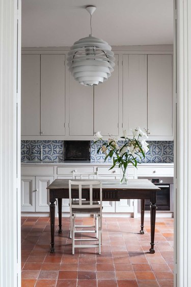 greige cabinets with patterned backsplash and terra cotta kitchen flooring