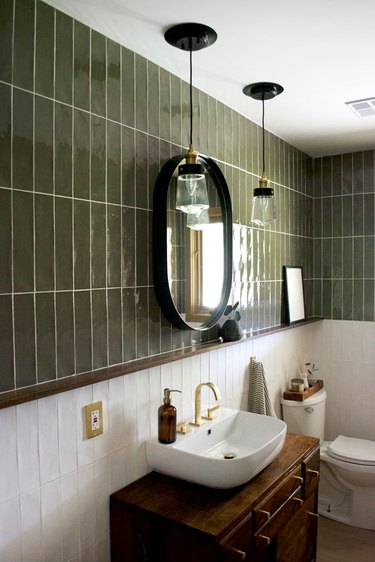 Bathroom with moss green and white tile backsplash, vessel sink, oval mirror, pendant lights.