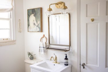 Bathroom with brass light and mirror, vintage oil painting, wooden towel ring and artisanal beads on hung on wall