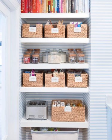 small pantry with woven storage bins and blue and white wallpaper