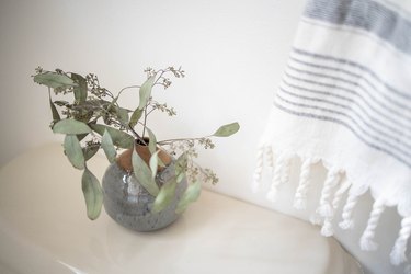 Small ceramic bud vase filled with eucalyptus on top of toilet