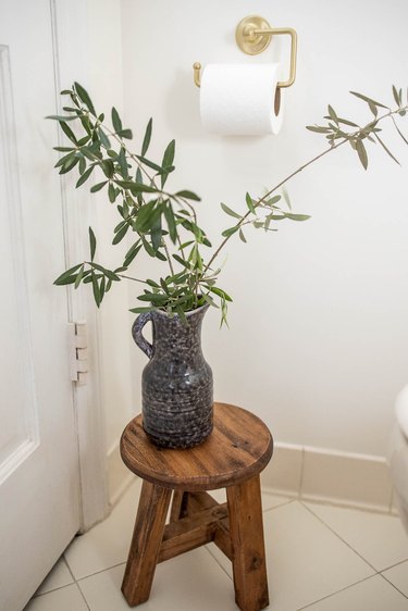Ceramic pitcher filled with olive leaves on top of rustic wooden stool