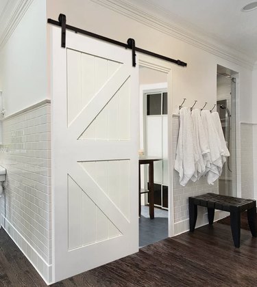 White Contemporary Barn Doors white subway tile, dark wood floors, black wood bench, white towels in hooks.