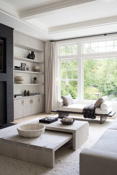 coastal living room with beige built in shelves, chaise lounge, gray wood nesting coffee tables, white beamed ceiling.