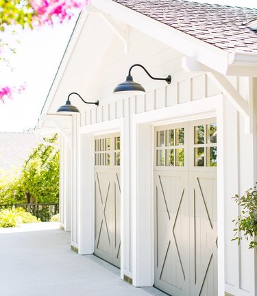 Cream barn garage doors with white exterior and black barn lights