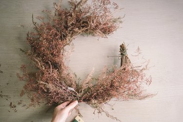 Attaching dried floral bundles to bottom half of crescent wreath