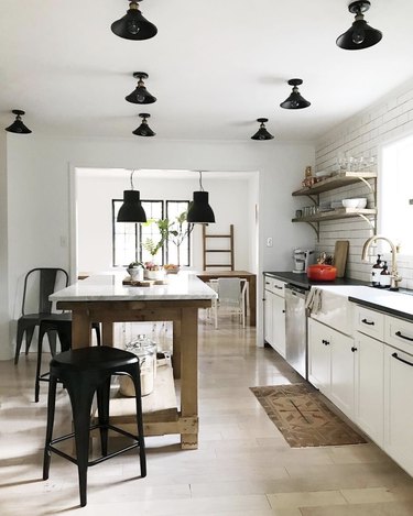 House Seven Design white kitchen with black ceiling lights and marble-topped island
