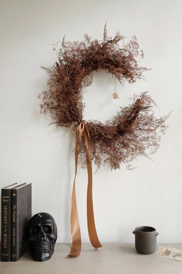 DIY crescent moon witch wreath with crystal on wall above Halloween decor