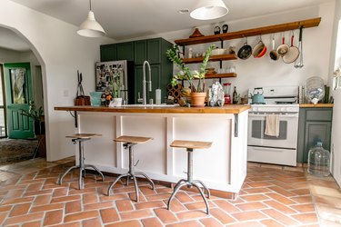 Brick herringbone kitchen floor with green cabinets and bohemian accents