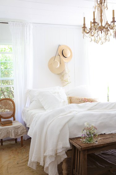 Crystal chandelier in French country bedroom with drapery at window and wooden bench at foot of the bed