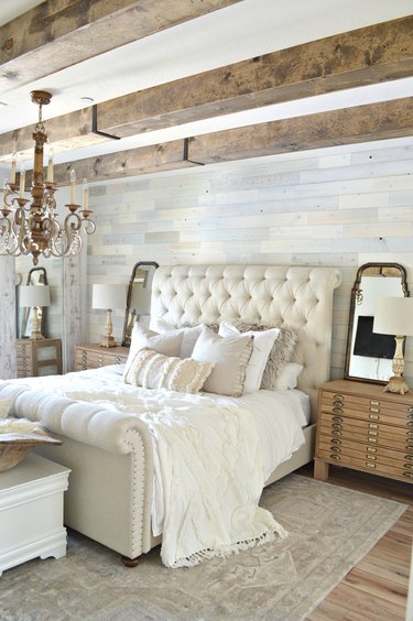 Soft textiles in French country bedroom with exposed wood beams and tufted headboard