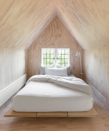 Scandinavian bedroom idea with floor-to-ceiling plywood "treehouse" with platform bed in front of window and modern floor lamp