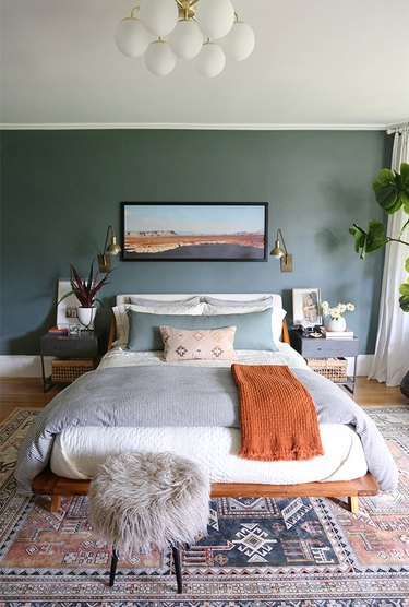 Bohemian bedroom style with green wall and faux fur stool at foot of bed