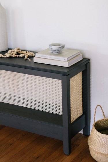 Black sideboard table with cane webbing, books and wood beads on top.