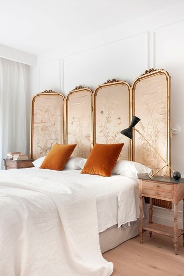 vintage bedroom style with ornate folding screen as headboard and antique nightstands with orange pillows