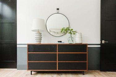 Round bedroom mirror hanging on wall above chest of drawers