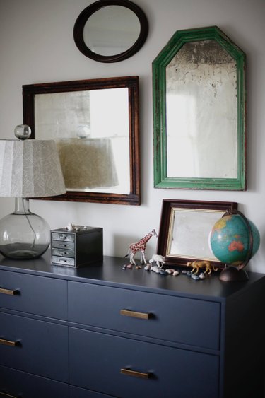 bedroom mirrors above blue dresser with table lamp and small accents