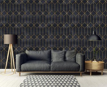 living room space with black couch and black and gold geometric wallpaper in the background