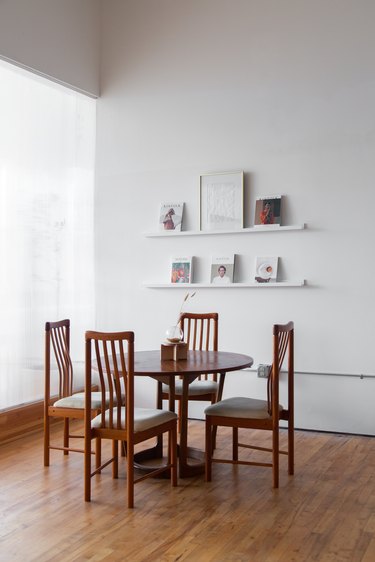 wood table and chairs with white shelves, magazines, and artwork nearby