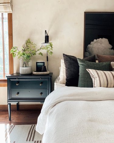 neutral bedroom with industrial wall sconce and painted black nightstand