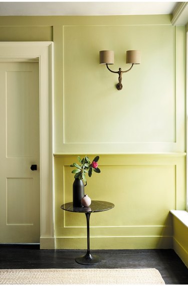 Hallway with wainscoting, paint, sconce, table.