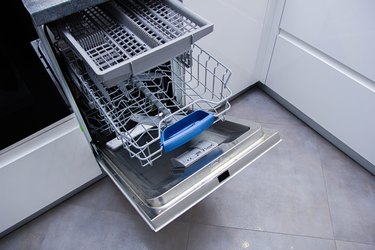 open modern dishwasher in the kitchen; built-in appliances in furniture.